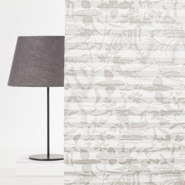 Beige Plissee mit floralen Mustern liegt gefaltet auf einer hellen Oberfläche. Die Falten sind gleichmäßig und die Textur erscheint leicht transparent. Das Plissee eignet sich für individuelle Fensterdekoration.