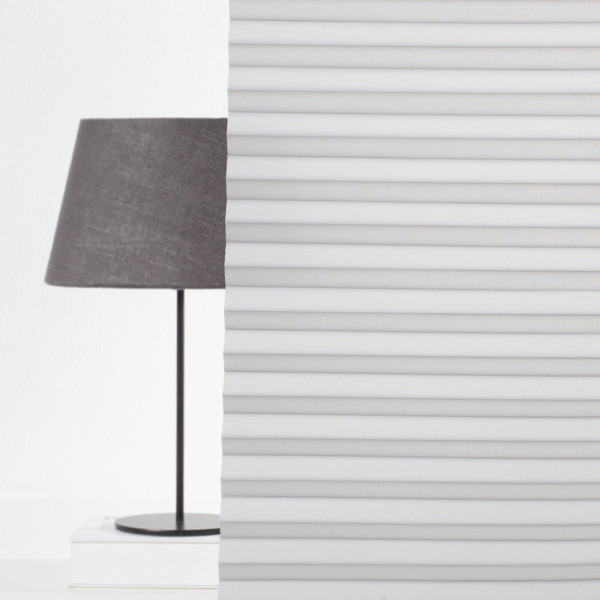 Grau gefaltetes Plissee mit strukturierter Oberfläche liegt auf einer weißen Fläche. Es hat gleichmäßige Falten und bietet halbtransparente Lichtfilterung.