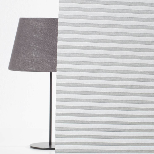 Weißes Wabenplissee Helgoland 3805 mit schwarzem Außenrand liegt flach auf einer Oberfläche. Es ist in gleichmäßige Falten gelegt und dient als verdunkelnder Sonnenschutz.