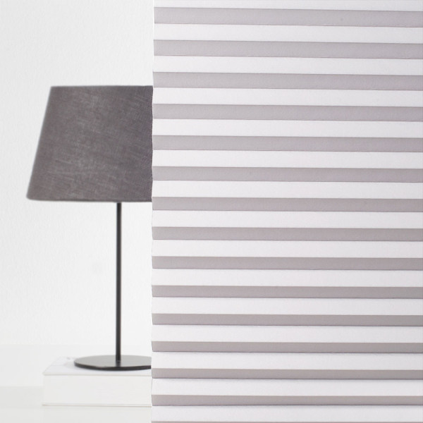 Plissee in Weiß mit strukturierter Oberfläche liegt gefaltet auf einem Untergrund. Es zeigt die verschiedenen Falten und die gleichmäßige Anordnung. Die Struktur ist gut sichtbar.