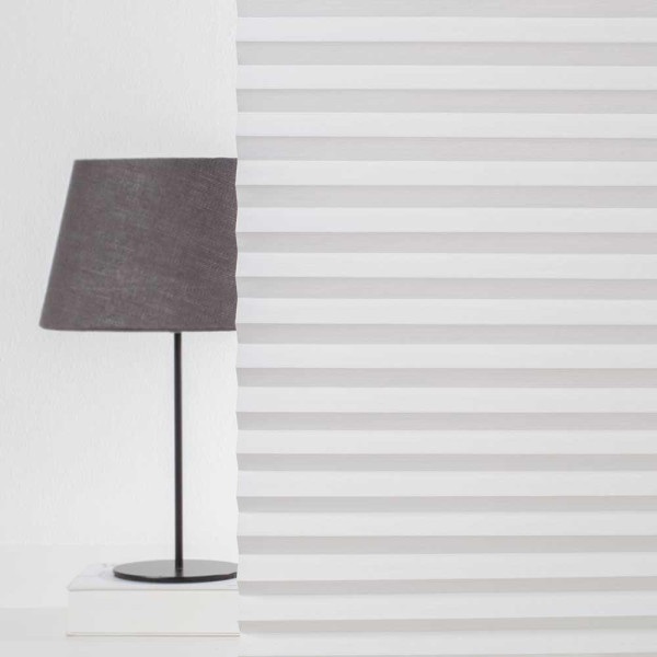 Weißes Plissee mit diagonal gefalteten Lamellen. Es zeigt eine gleichmäßige Struktur und lässt Licht durch, während es dennoch Sichtschutz bietet. Die Oberfläche wirkt elegant und schick.
