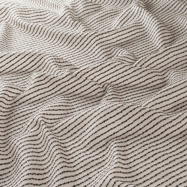 Halbtransparenter Dekostoff mit feinen schwarzen Streifen auf hellem Hintergrund liegt unordnet auf einer Fläche. Der Stoff hat eine weich fließende Textur.