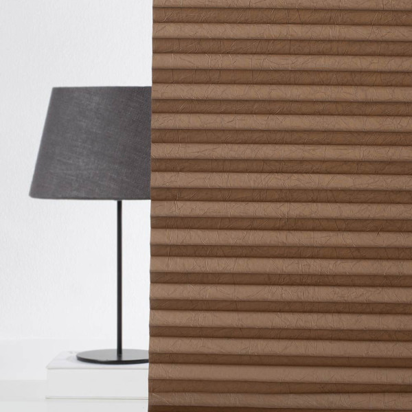 Braunes Plissee mit gefalteter Struktur liegt flach auf einer weißen Oberfläche. Die Falten sind gleichmäßig und subtil, passend für individuelle Fensterdekoration.