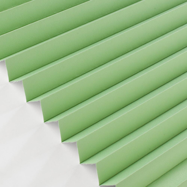 Grüne Plissee-Vorhänge sind gefaltet und bilden eine gleichmäßige Struktur. Sie sind auf einem hellen Untergrund angebracht und dienen der Verdunkelung.