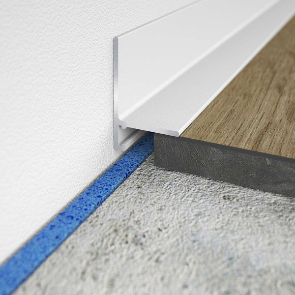 Minileiste Sockelprofil SL 16X5 in Weiß liegt bündig am Boden an. Der Übergang zwischen dem Holz- und Betonboden ist deutlich sichtbar. Ein blauer Dichtstreifen ist erkennbar.