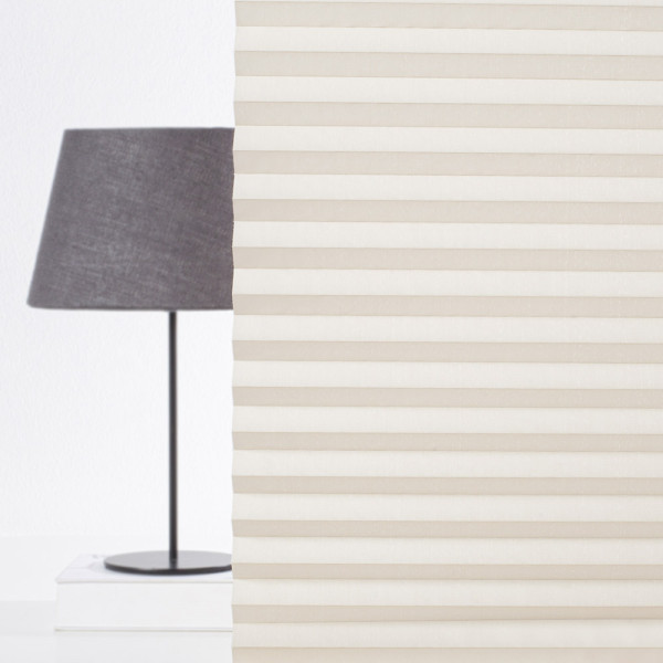 Halbtransparentes Plissee in sanften Naturtönen liegt gefaltet auf einer Oberfläche. Die Stoffstruktur zeigt regelmäßige Falten und wirkt elegant, während die Lichtdurchlässigkeit angedeutet wird.