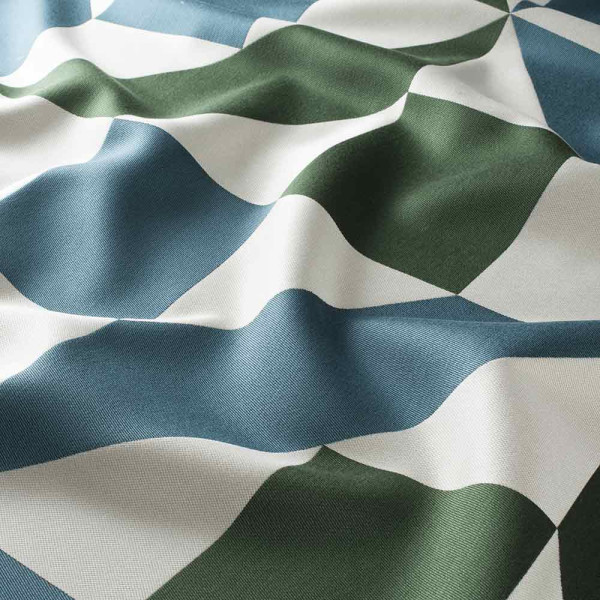 Blaue, grüne und weiße geometrische Muster prägen den weich fallenden Vorhangstoff. Der Stoff hat eine glatte Oberfläche und zeigt eine sanfte Wellenstruktur durch die Drapierung.
