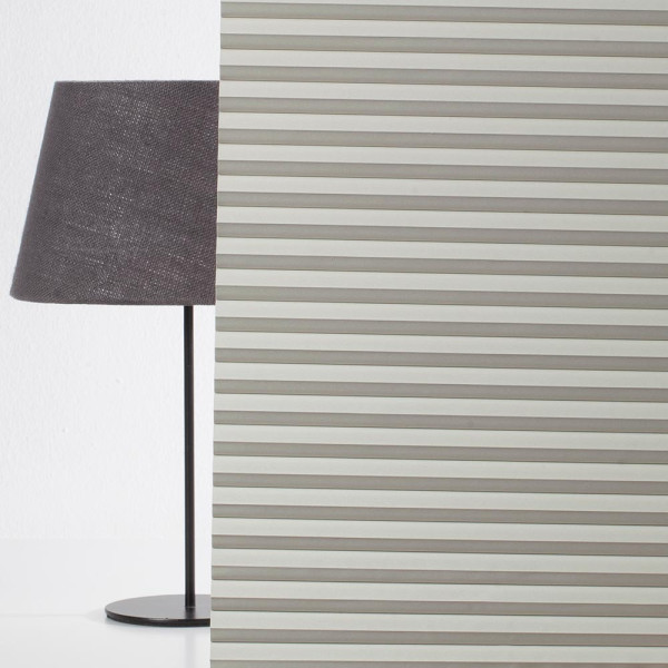 Graue Lampe mit schwarzem Lampenschirm steht neben einer vertikal gestreiften Wandverkleidung. Die Streifen sind in einem hellen Farbton gehalten und vermitteln einen modernen Look.