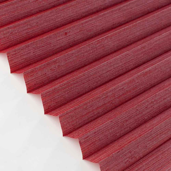 Rotes Plissee in Wellenform liegt quer auf einer Oberfläche. Das Plissee ist blickdicht und aus hochwertigen Materialien gefertigt. Es wird für individuelle Anfertigungen angeboten.