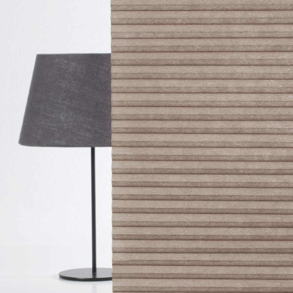 Beige Wabenplissee mit vertikalen Längsstreifen steht an einer Wand neben einer Schreibtischlampe mit schwarzem Lampenschirm. Der Raum wirkt modern und minimalistisch.