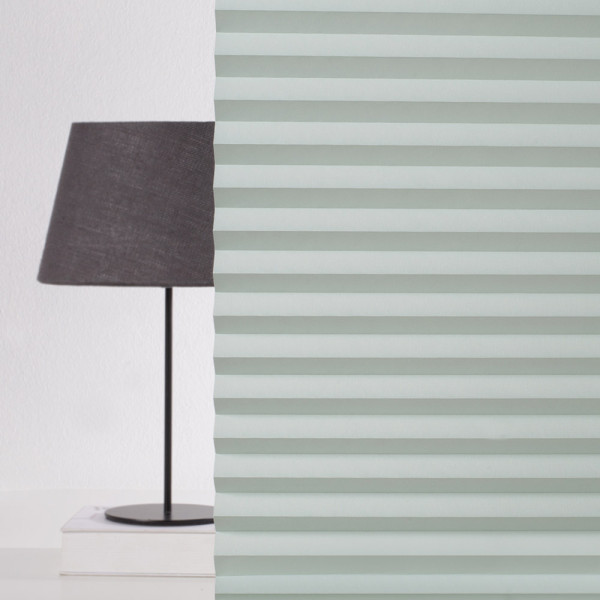 Grüne, gefaltete Plissee-Jalousien zeigen gleichmäßige, senkrechte Falten. Die Struktur sorgt für eine blickdichte Abdeckung und lichtdurchlässigen Effekt. Sie sind auf einem weißen Untergrund angeordnet.