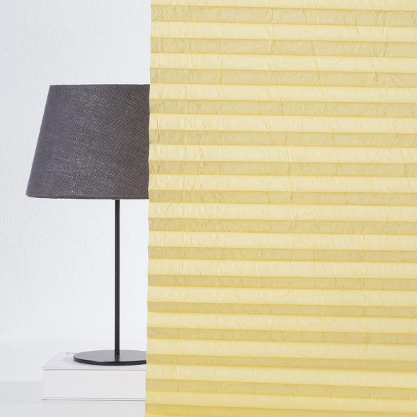 Plissee in gelber Farbe zeigt eine strukturierte, gefaltete Oberfläche. Die Falten sind gleichmäßig angeordnet und reflektieren sanftes Licht. Das Material wirkt blickdicht und hochwertig.