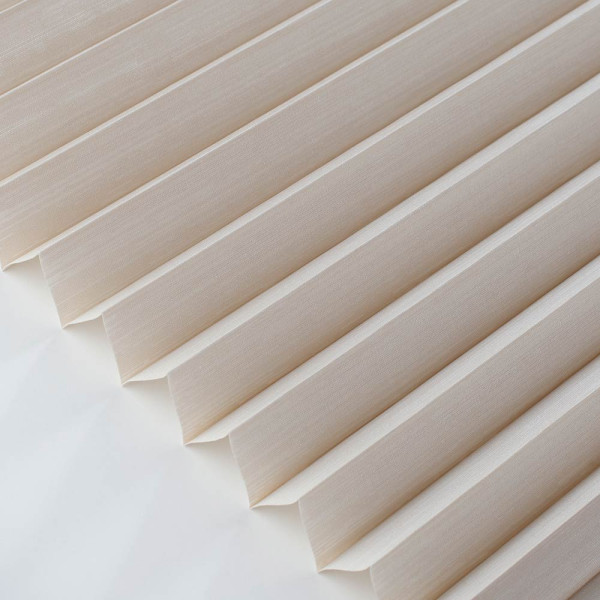 Beige Plissee mit wellenförmigem Muster liegt auf einem weißen Hintergrund. Die Falten sind gleichmäßig und verleihen dem Stoff eine elegante Textur.