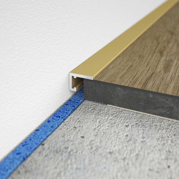 Goldenes Abschlussprofil AL 10X5 schließt den Übergang zwischen Holzboden und Wand ab. Der obere Teil ist glatt und glänzend, während der untere Teil rau ist.