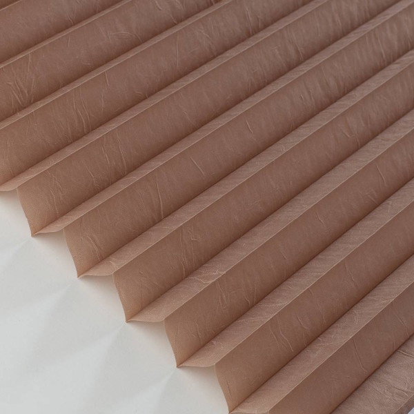 Hellbraunes Plissee mit gefalteter Struktur liegt auf hellen Untergrund. Die Falten sind gleichmäßig und verleihen dem Stoff ein modernes Aussehen. Das Plissee ist blickdicht und maßgefertigt.