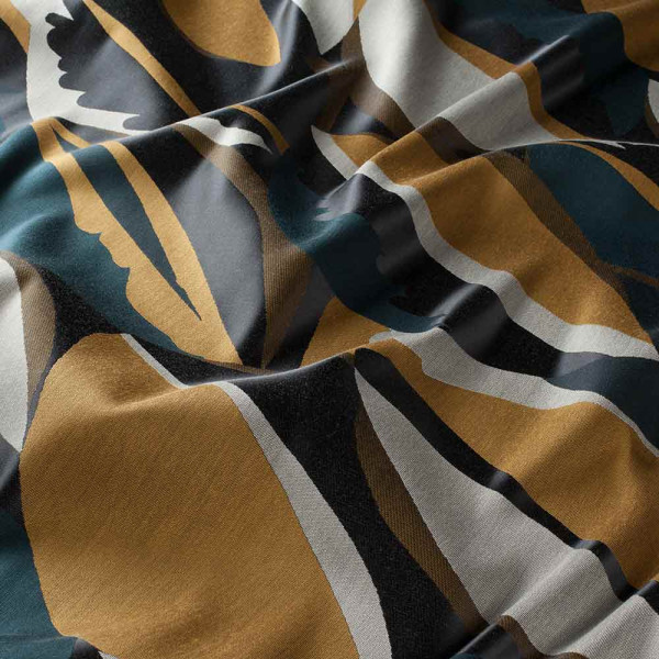 Dekostoff mit einem spielerischen, geschwungenen Muster in Braun-, Blau- und Grautönen liegt faltenwurfartig. Die Farben verlaufen harmonisch und verbinden sich zu einem ansprechenden Design.