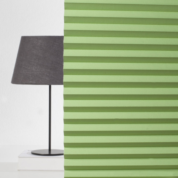 Grüne Plissee-Vorhänge sind gefaltet und bilden eine gleichmäßige Struktur. Sie sind auf einem hellen Untergrund angebracht und dienen der Verdunkelung.