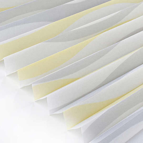 Halbtransparentes Plissee Wyk 7583 in sanften Gelb- und Grautönen liegt gefaltet auf einer glatten Oberfläche. Die Stoffstruktur ist gut erkennbar und vermittelt ein elegantes Erscheinungsbild.