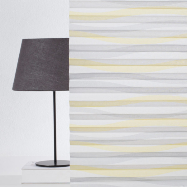 Halbtransparentes Plissee Wyk 7583 in sanften Gelb- und Grautönen liegt gefaltet auf einer glatten Oberfläche. Die Stoffstruktur ist gut erkennbar und vermittelt ein elegantes Erscheinungsbild.