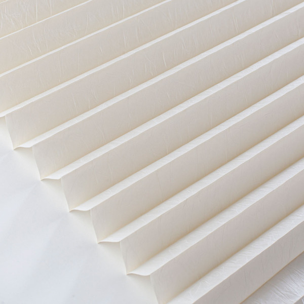 Cremefarbenes Plissee mit gleichmäßigen Falten ist auf einem hellen Hintergrund sichtbar. Es präsentiert sich als Sichtschutz für Fenster und kann nach Maß gefertigt werden.