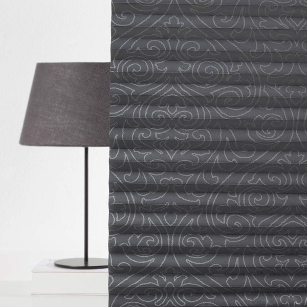 Dunkelgraues Plissee mit floralem Muster liegt gefaltet auf einem weißen Untergrund. Die Falten sind gleichmäßig angeordnet und erzeugen eine strukturierte Optik.