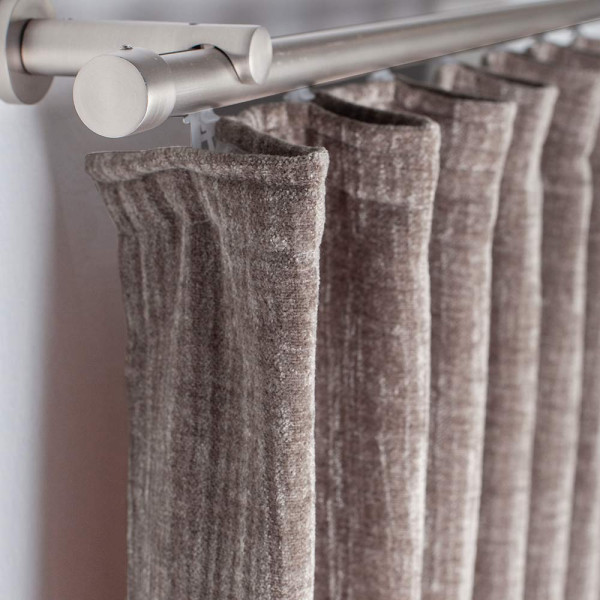 Wärmedämmender Vorhang INUIT aus schwerem Stoff, dunkelbraun mit einer dekorativen Faltenlegung oben, hängt an einer silbernen Gardinenstange.